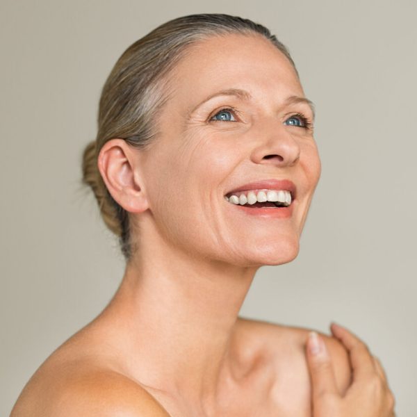 Portrait of a cheerful senior woman smiling while looking away isolated on gray background. Happy mature woman after spa massage and anti-aging treatment on face.